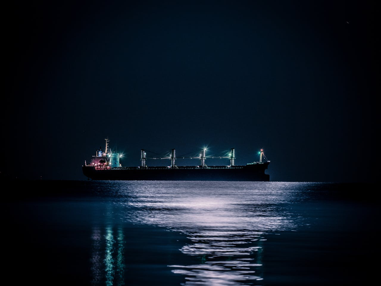 services-01 A tranquil nighttime scene of a cargo ship floating on a calm ocean under a starlit sky.